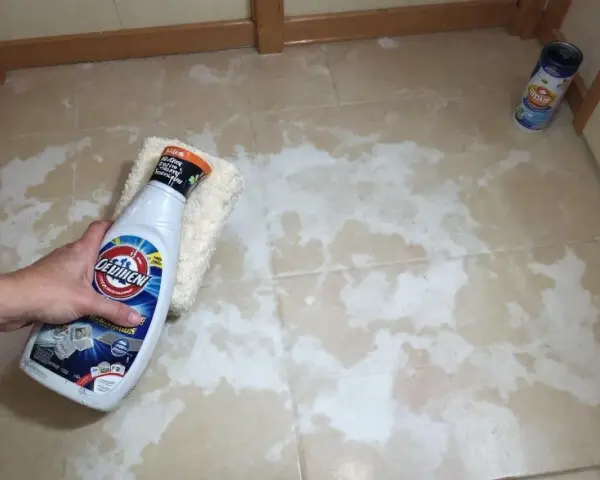 Main tenant tente de nettoyer un voile de ciment qui ne part pas sur le carrelage avec un produit.