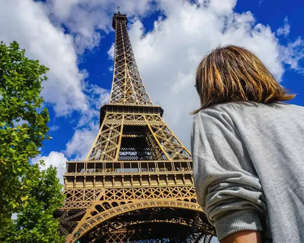 Persona admira la imponente Torre Eiffel bajo un cielo azul con nubes.