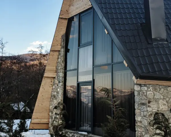 Moderna ristrutturazione casa di montagna: tetto scuro, ampie vetrate con vista sui monti, pietra e legno.