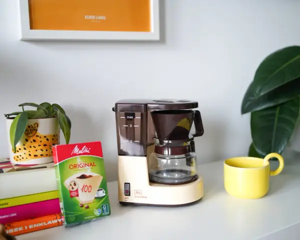 Kawiarka przelewowa Melitta Aromaboy gotowa do zaparzenia porannej kawy. Obok filtry i żółta filiżanka.