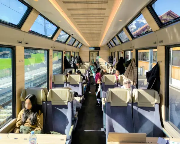 Passengers enjoy the scenic views from the panoramic windows of a train on the Golden Pass Line, with mountains visible outside.