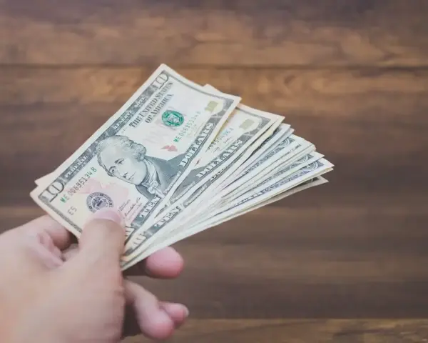 Dłoń trzyma plik banknotów dziesięciodolarowych. To może być zapłata za trzynastkę lub po prostu nagroda.