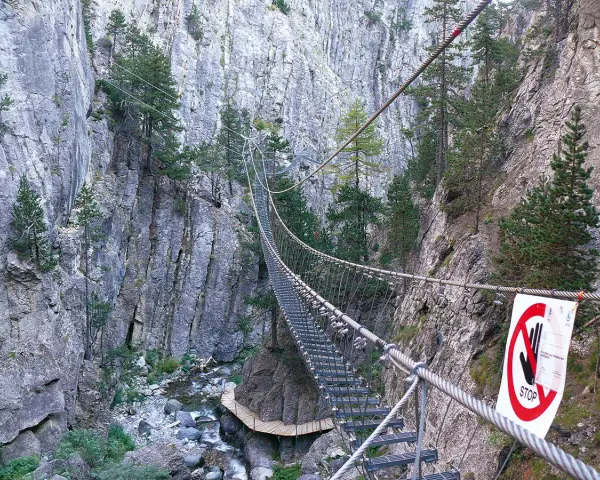 Un emozionante ponte tibetano in Piemonte attraversa una gola rocciosa, con un torrente sottostante e pini aggrappati alle pareti.