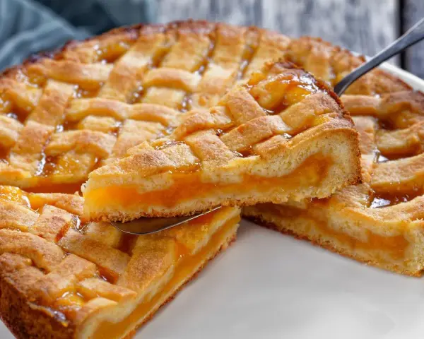 Deliziosa crostata senza glutine con ripieno di albicocche, la fetta sollevata mostra la morbidezza dell'impasto e la succosità della frutta.