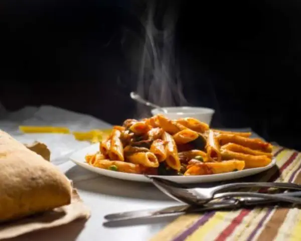 Piatto fumante di penne alla vodka, con pane croccante e posate. Un classico confortante.
