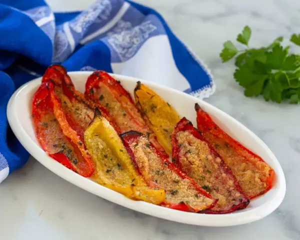 Peperoni gratinati al forno, rossi e gialli, cotti alla perfezione con pangrattato e erbe aromatiche, serviti su un piatto bianco con un tovagliolo blu.