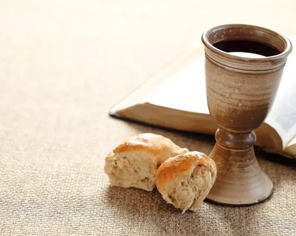 Kelch mit Rotwein, Brot und aufgeschlagenes Buch. Symbol für das christliche Abendmahl und dessen Bedeutung im Glauben.