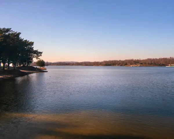 Spokojne jeziora w Małopolsce o zachodzie słońca. Drzewa na brzegu rzucają długie cienie na piaszczystą plażę.