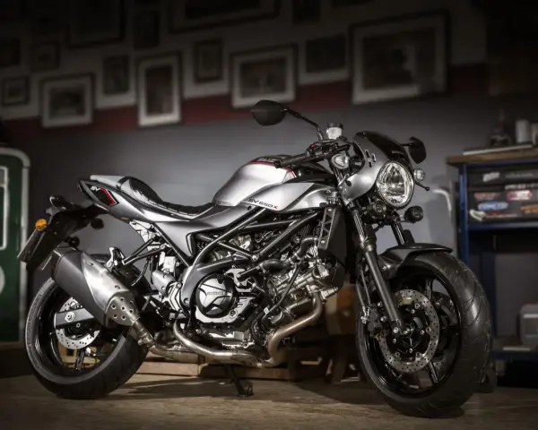Srebrny motocykl Suzuki SV650X z czarną ramą i detalami, stojący w garażu.