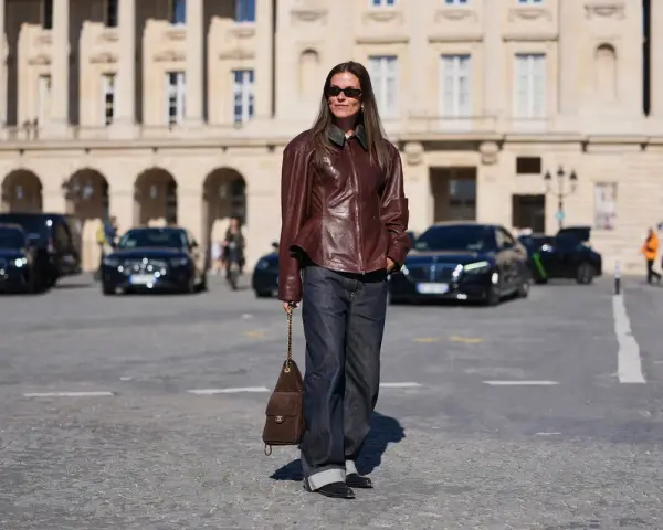 Elegancka kobieta w skórzanej kurtce i jeansach, z brązową torebką na ramieniu. Jej filigranowa figura podkreślona jest przez luźne spodnie i dopasowaną górę.