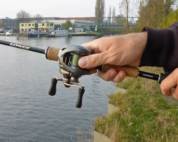 Hand hält Angelrute mit Baitcast-Rolle, die grüne baitcast schnur ist gut sichtbar.