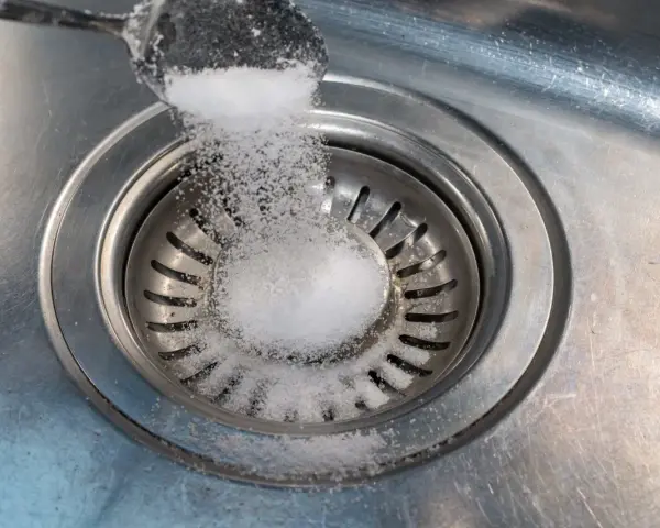 Salt hälls ner i diskhoavloppet. En skopa med salt sprids över silen.