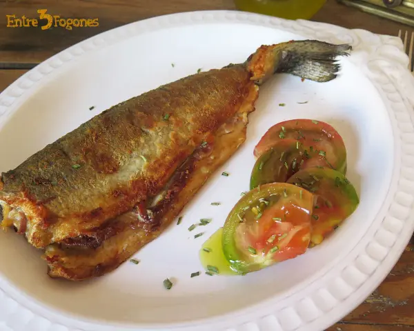 Trucha a la navarra dorada y crujiente, servida con rodajas de tomate fresco y hierbas aromáticas.