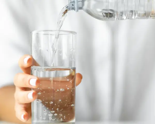 Eine Hand hält ein Glas, in das kohlensäurehaltiges Mineralwasser gegossen wird.