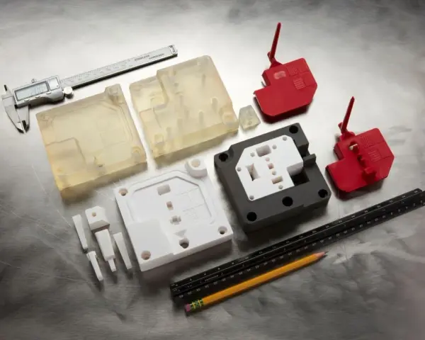 Various 3d printed molds, including clear, white, and red plastic components, are laid out with a caliper, ruler, and pencil on a metallic surface.