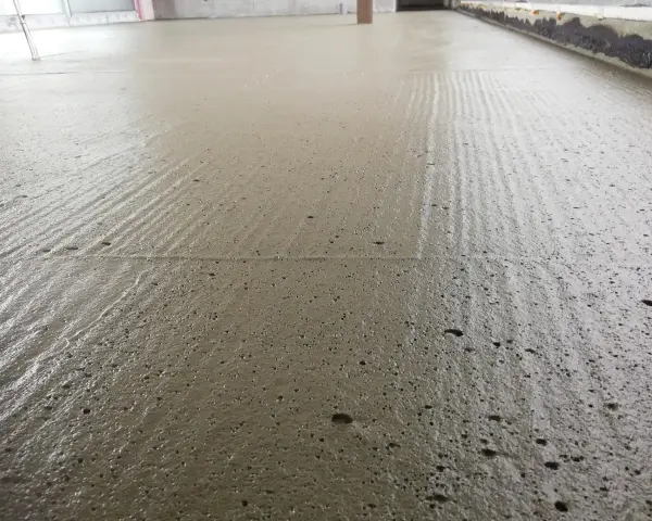 Świeżo wylany, wilgotny **pianobeton** na budowie, z widocznymi śladami po zacieraniu i drobnymi pęcherzykami powietrza.