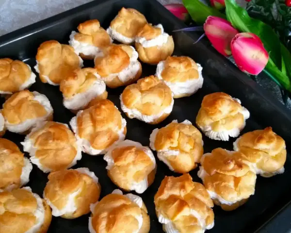 Pyszne ciasto na ptysie, wypełnione kremem, czeka na spróbowanie. Obok piękne tulipany.