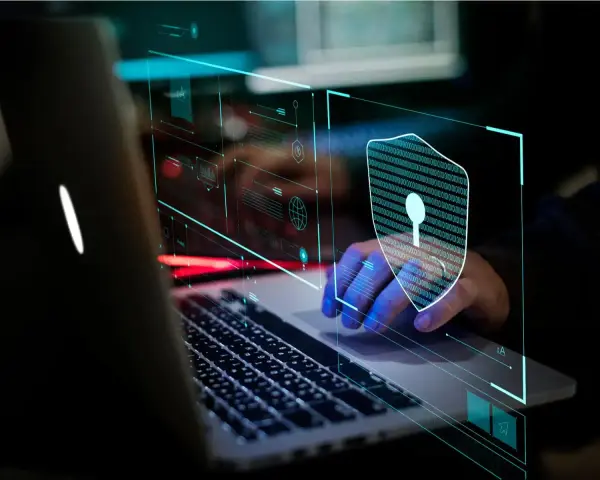 Mano sobre teclado de portátil, con un escudo digital de ceros y unos, simbolizando la seguridad informática.