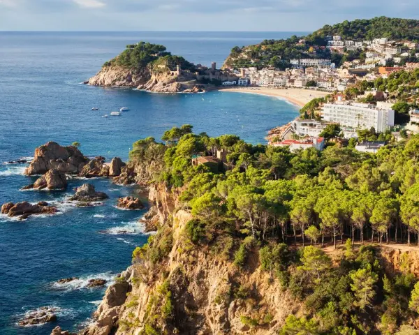 Scenic view of the Costa Brava coastline, a perfect stop on the way to Barcelona, with rugged cliffs, pine forests, and a charming town nestled by the sea.