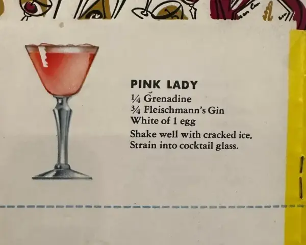 Elegancki kieliszek z różowym drinkiem Pink Lady, obok przepis na jego przygotowanie: grenadyna, gin i białko jaja.