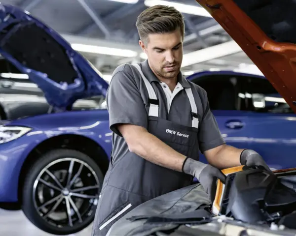 Mechaniker mit BMW Service Kleidung arbeitet an einem blauen BMW. Transparente Kosten für BMW Service.