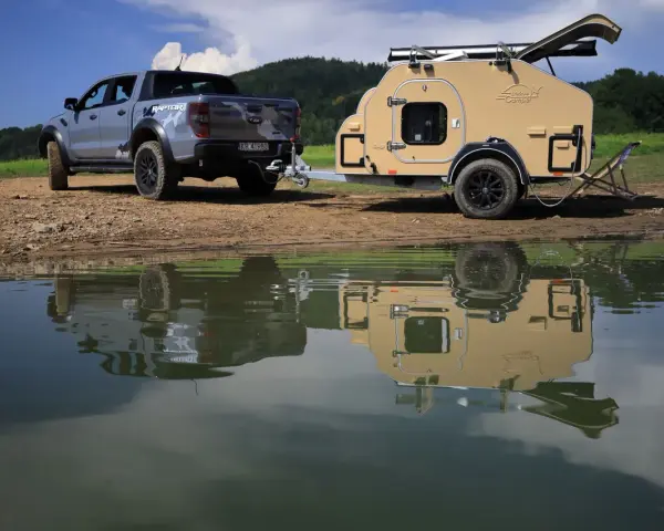 Srebrny Ford Raptor z przyczepą wyprawową Lifestyle Camper nad jeziorem.