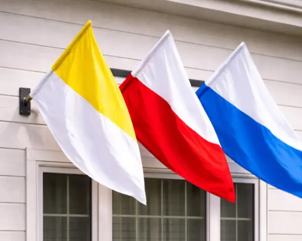 Trzy flagi: żółto-biała, czerwono-biała i niebiesko-biała, powiewają na wietrze. To może być flaga kościelna lub symbol parafii.