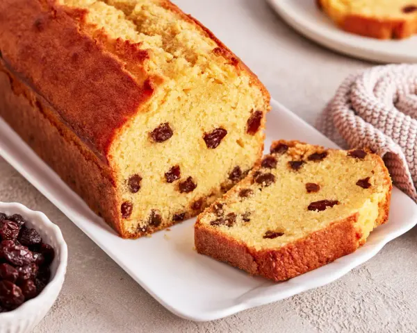 Ein saftiger Rosinenkuchen mit goldbrauner Kruste, auf einem weißen Teller angerichtet. Rosinen sind gut sichtbar im Teig verteilt.