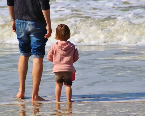 Ojciec i dziecko na plaży, cieszący się wspólnym urlopem ojcowskim 9 tygodni.