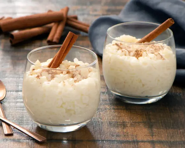 Dos copas de cremoso arroz con leche, espolvoreado con canela y decorado con una rama de canela.