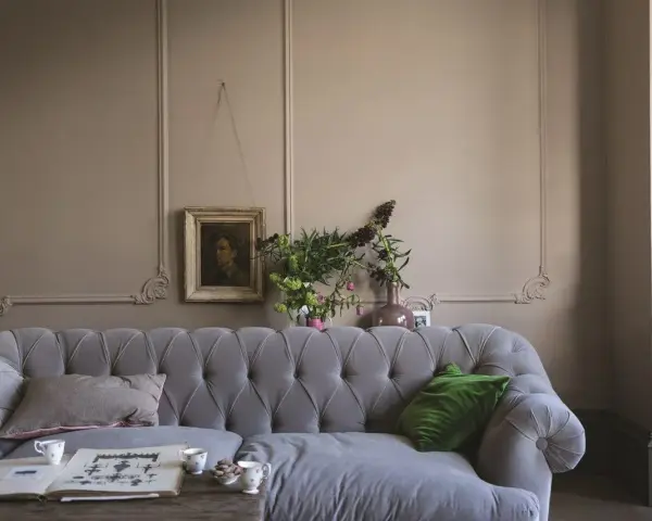 Szara kanapa w salonie z obrazem i bukietem kwiatów. Dominują **kolory ziemi**, tworząc przytulną atmosferę.
