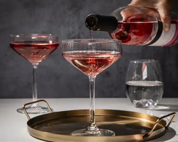 Różowe wino nalewane do kieliszków. Zastanawiasz się, jakie kieliszki do jakiego wina? Tutaj widzimy kieliszki typu coupe, idealne do lekkich win musujących.