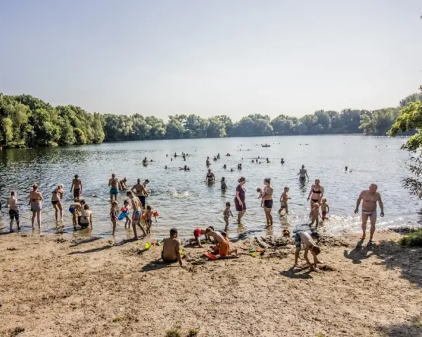 Menschen genießen einen sonnigen Tag im Strandbad Hamburg. Kinder spielen im Sand, während Erwachsene im Wasser planschen.
