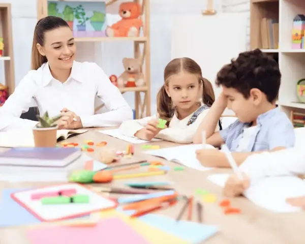 Uśmiechnięta nauczycielka przygląda się dzieciom podczas lekcji. To idealne miejsce na podanie o pracę nauczyciel.