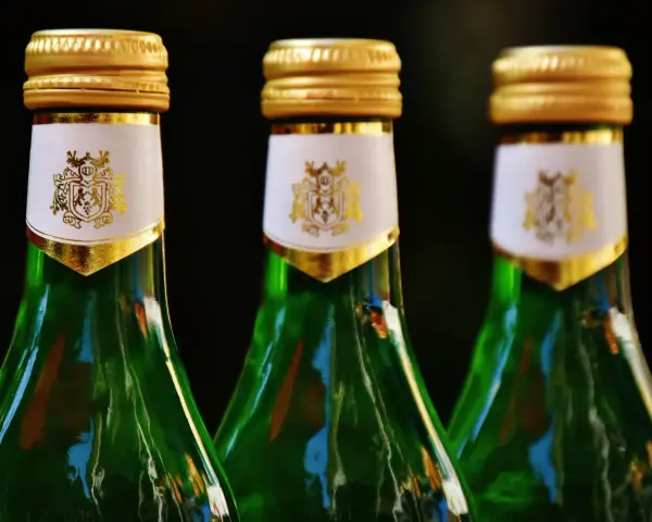 Trzy zielone butelki z złotymi nakrętkami i białymi etykietami z herbem. Zastanawiasz się, absynt co to?