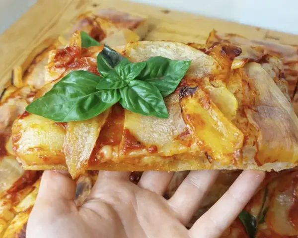 Una fetta di pizza di patate dorata, guarnita con basilico fresco, pronta per essere gustata.
