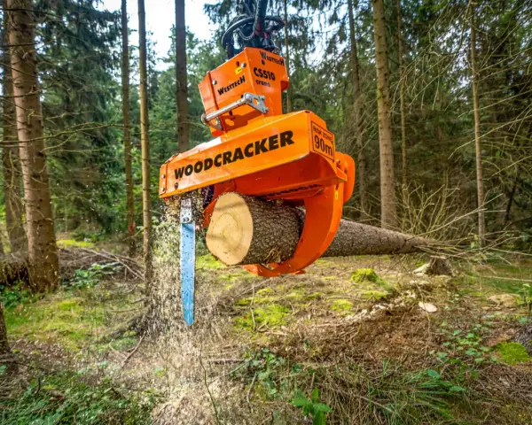 Pomarańczowe maszyny leśne do zrywki drewna, model Woodcracker, tną pień drzewa w lesie.