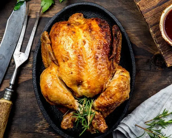 Pollo al horno dorado y jugoso, servido en sartén de hierro fundido con romero. Acompañado de salsa barbacoa y cubiertos rústicos.