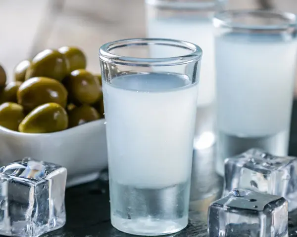 Raki, ein Getränk, das oft mit Griechenland assoziiert wird, wird aus Trauben hergestellt. Hier sind Gläser mit Raki, Eiswürfel und Oliven.