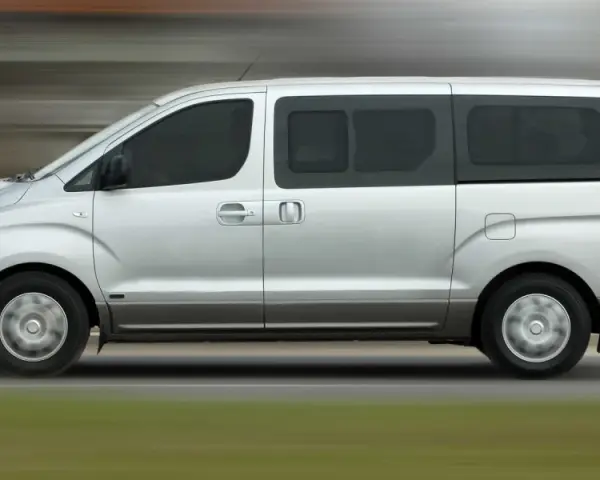 Un mini bus argenté roule sur une route. Ce véhicule spacieux est idéal pour les familles ou les groupes, et peut être conduit avec un permis B.