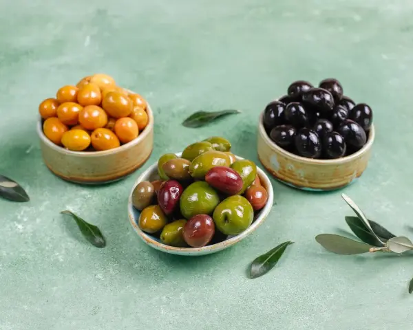 Tres cuencos con aceitunas de diferentes colores: amarillas, verdes y negras.