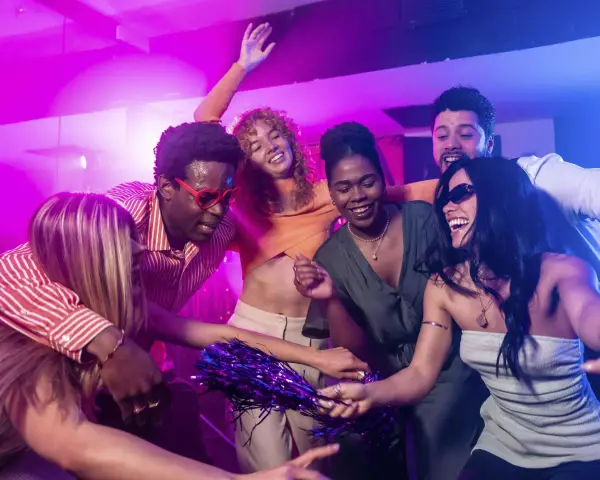 Fröhliche Freunde tanzen ausgelassen zu ihrer **dance music playlist** im Club, umgeben von lila und blauer Beleuchtung.