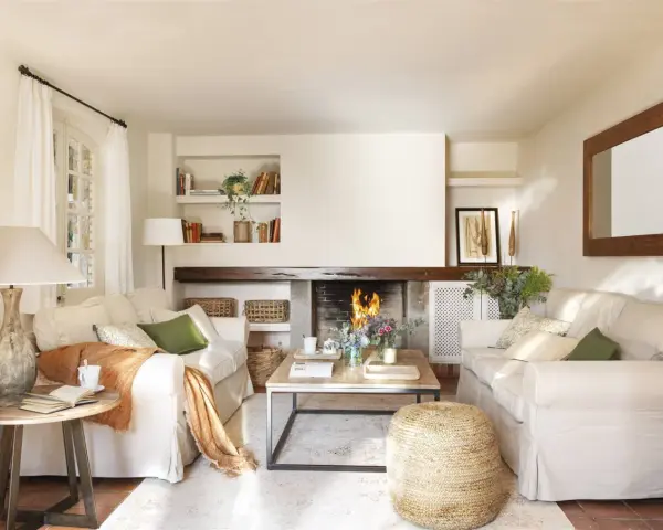 Salón acogedor con chimenea encendida, sofás blancos, mesa de centro de madera y detalles decorativos.