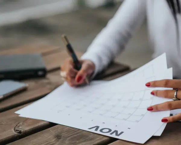 Une main avec des ongles rouges écrit sur un calendrier, planifiant peut-être la date de mariage. Un téléphone et un carnet sont à proximité.