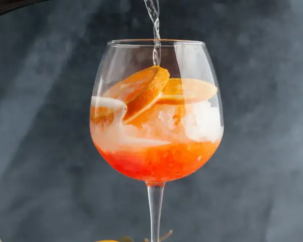 Orzeźwiający drink z cydrem, lodem i plasterkami pomarańczy, przygotowywany w dużym kieliszku.
