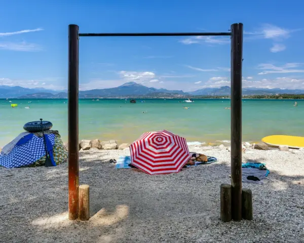 Słoneczne plaże nad Jeziorem Garda, z turkusową wodą, górami w tle i kolorowymi parasolami.
