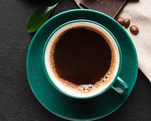 Aromatic coffee in a green cup, next to chocolate and beans. Czy kawa podnosi kortyzol? This morning brew might be the answer.