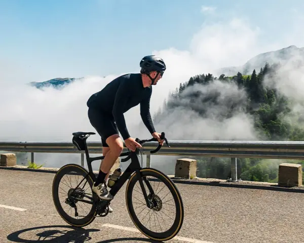 A cyclist in black gear conquers a mountain road, enjoying the breathtaking views and the freedom of long rides amidst swirling clouds.