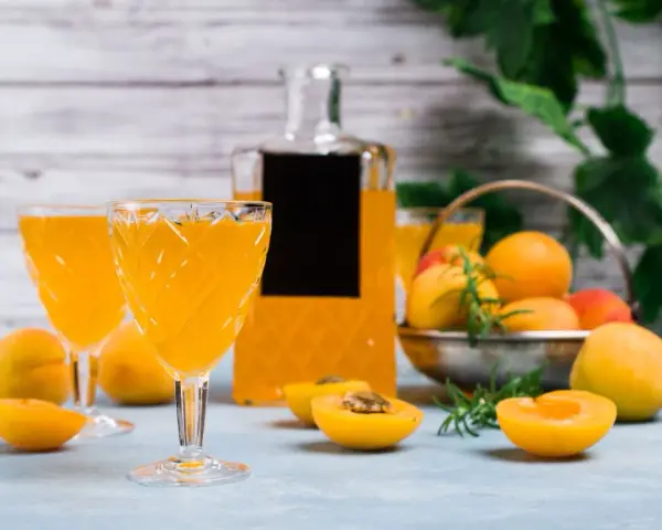 Orzeźwiający drink z likierem brzoskwiniowym, podany w eleganckich kieliszkach, z owocami i butelką w tle.