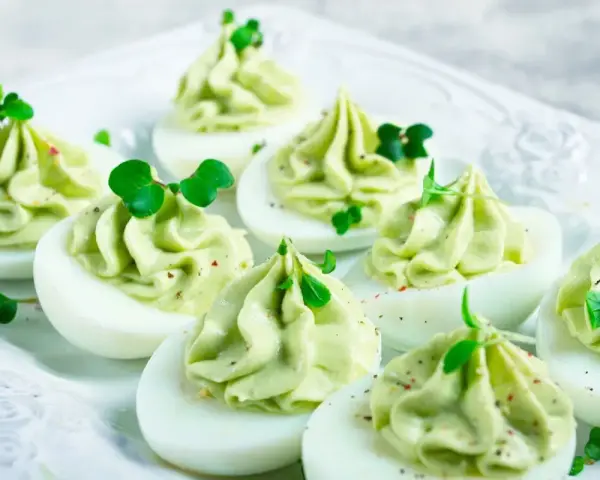 Uova ripiene pasquali, guarnite con crema verde e germogli freschi, pronte per essere gustate.